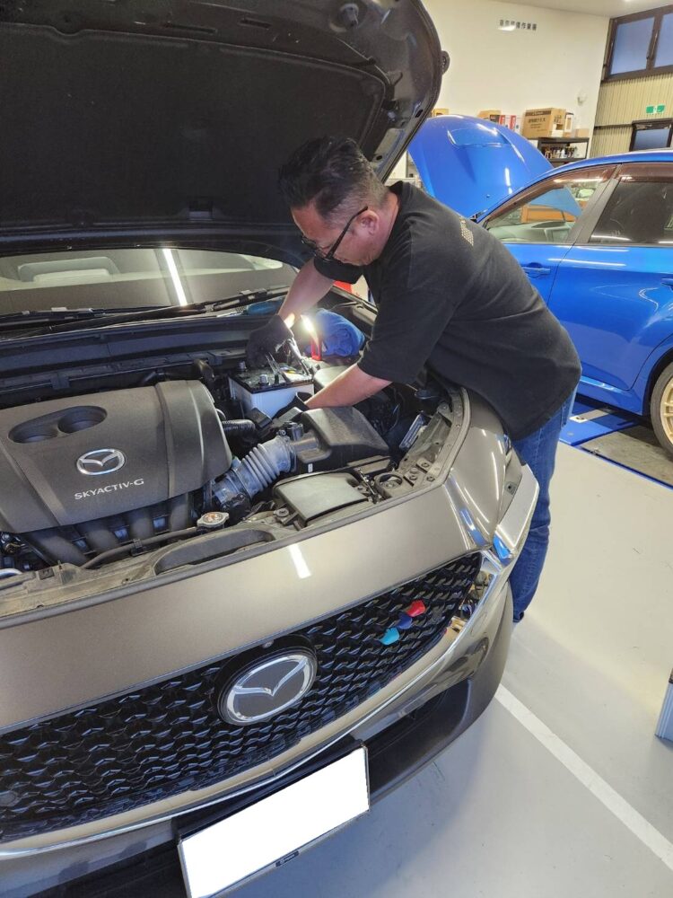 CX-30のエンジンルームでバッテリー交換作業をするスタッフ